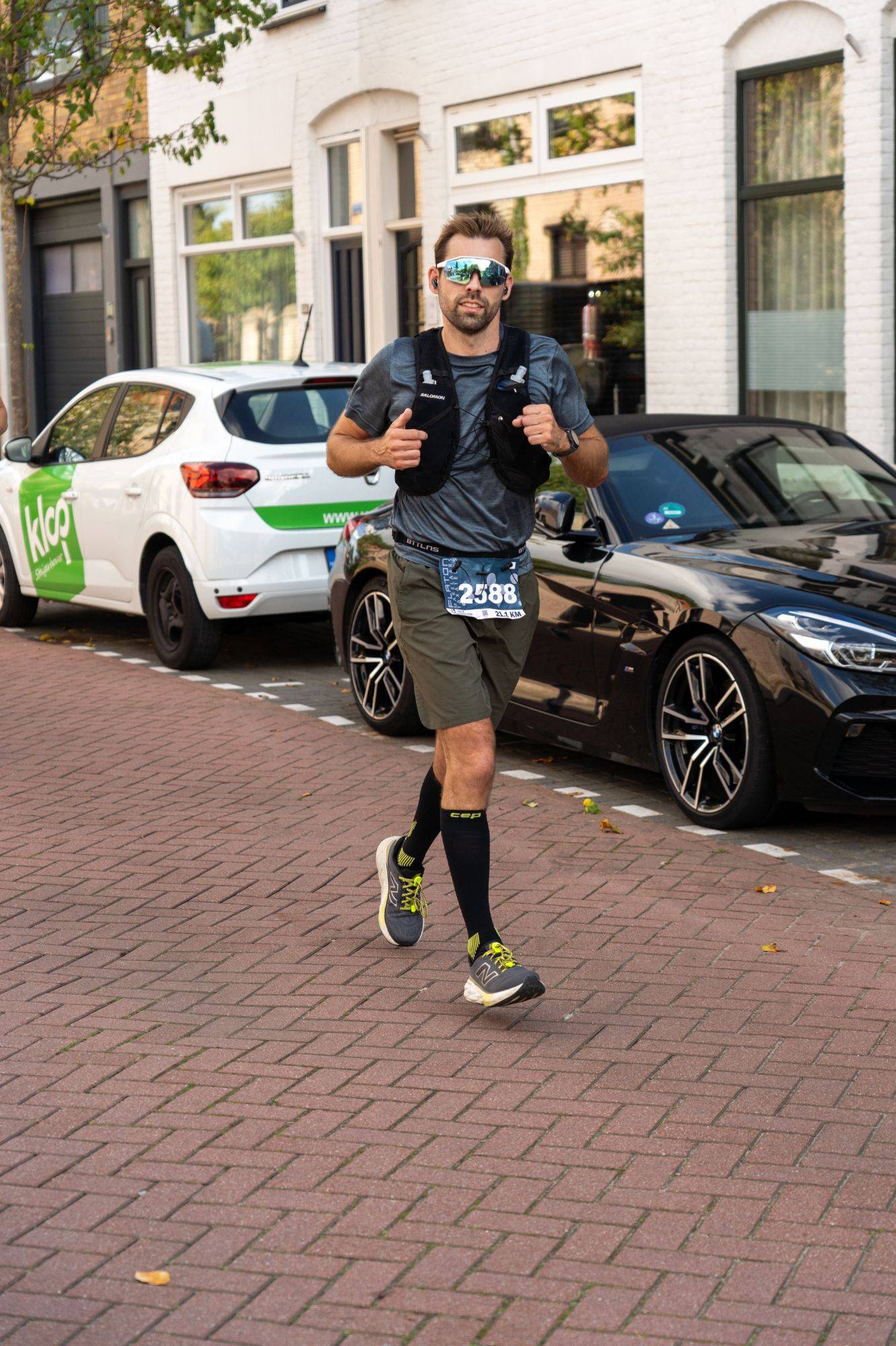 Edwin running through a town street in a half marathon, wearing sunglasses, a running vest and bib 2588.