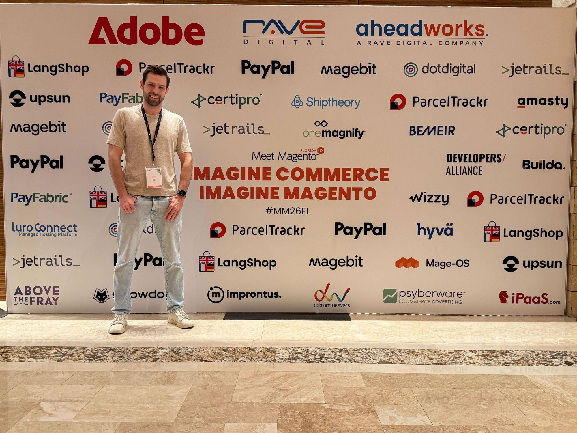 Edwin standing in front of the sponsor wall at Meet Magento Florida, reading Imagine Commerce, Imagine Magento.